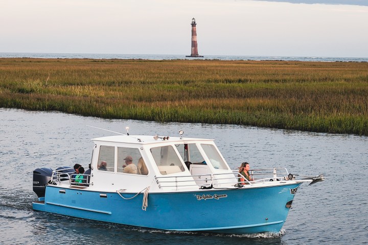 Blue boat on water with lighthouse in background