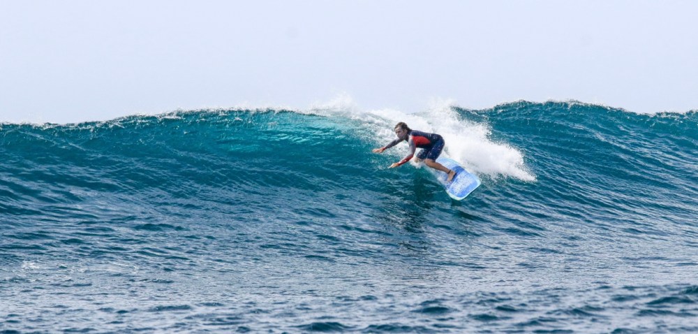 Person surfing on a wave in the ocean under a clear sky.