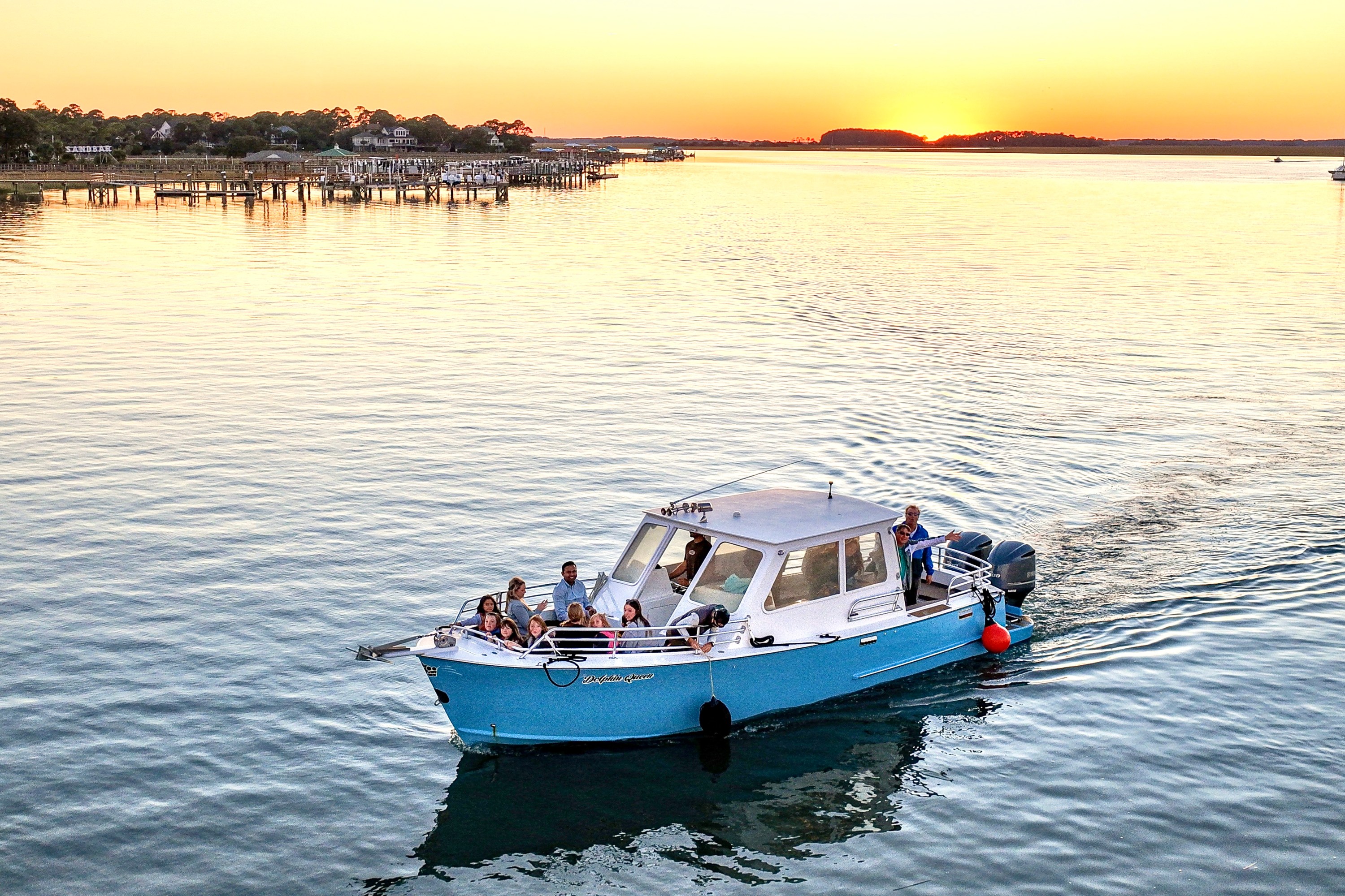 Small blue boat with people on calm water at sunset.