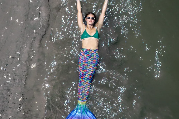 Mermaid lies on beach, arms outstretched.