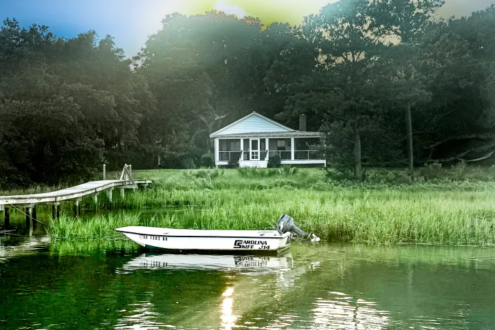 Boat on water near grassy shore with a house in the background.