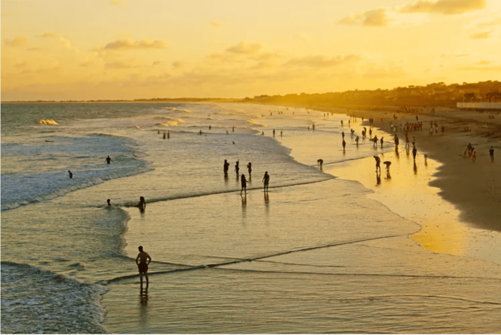 People enjoying a sunset on a beach with waves and a golden sky.