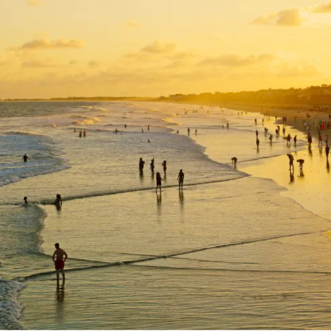 People enjoying a sunset on a beach with waves and a golden sky.