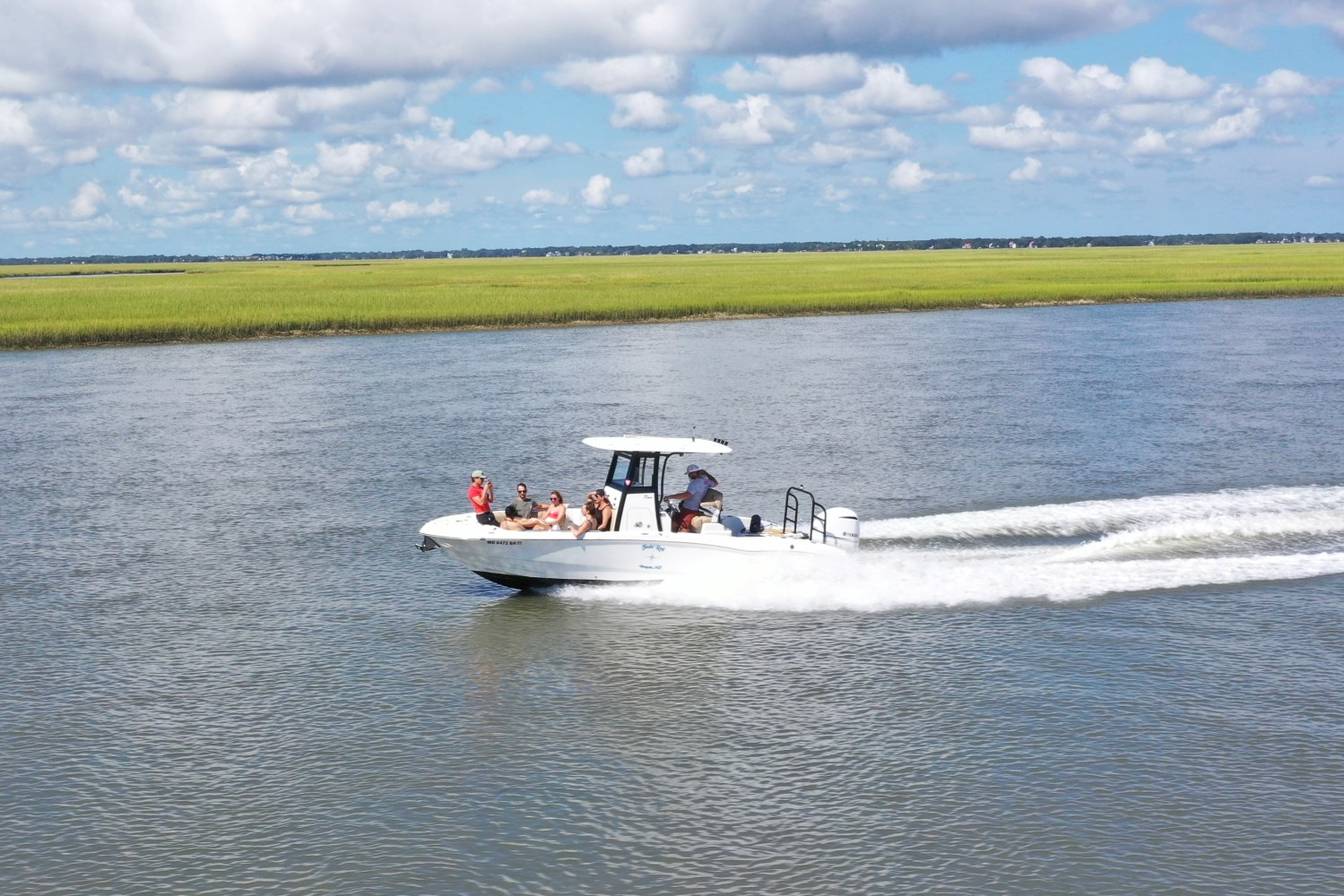 Boat with people cruising on a river under a cloudy sky.