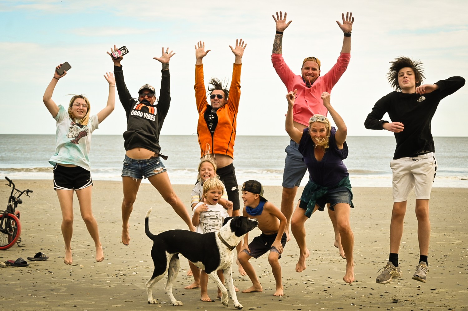 Group of people and a dog jumping joyfully on a beach.