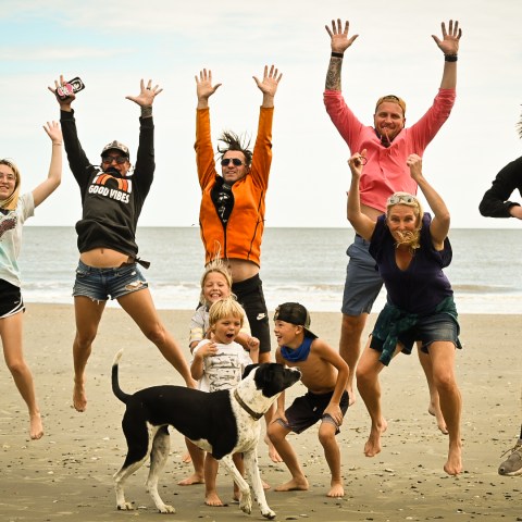 Group of people and a dog jumping joyfully on a beach.