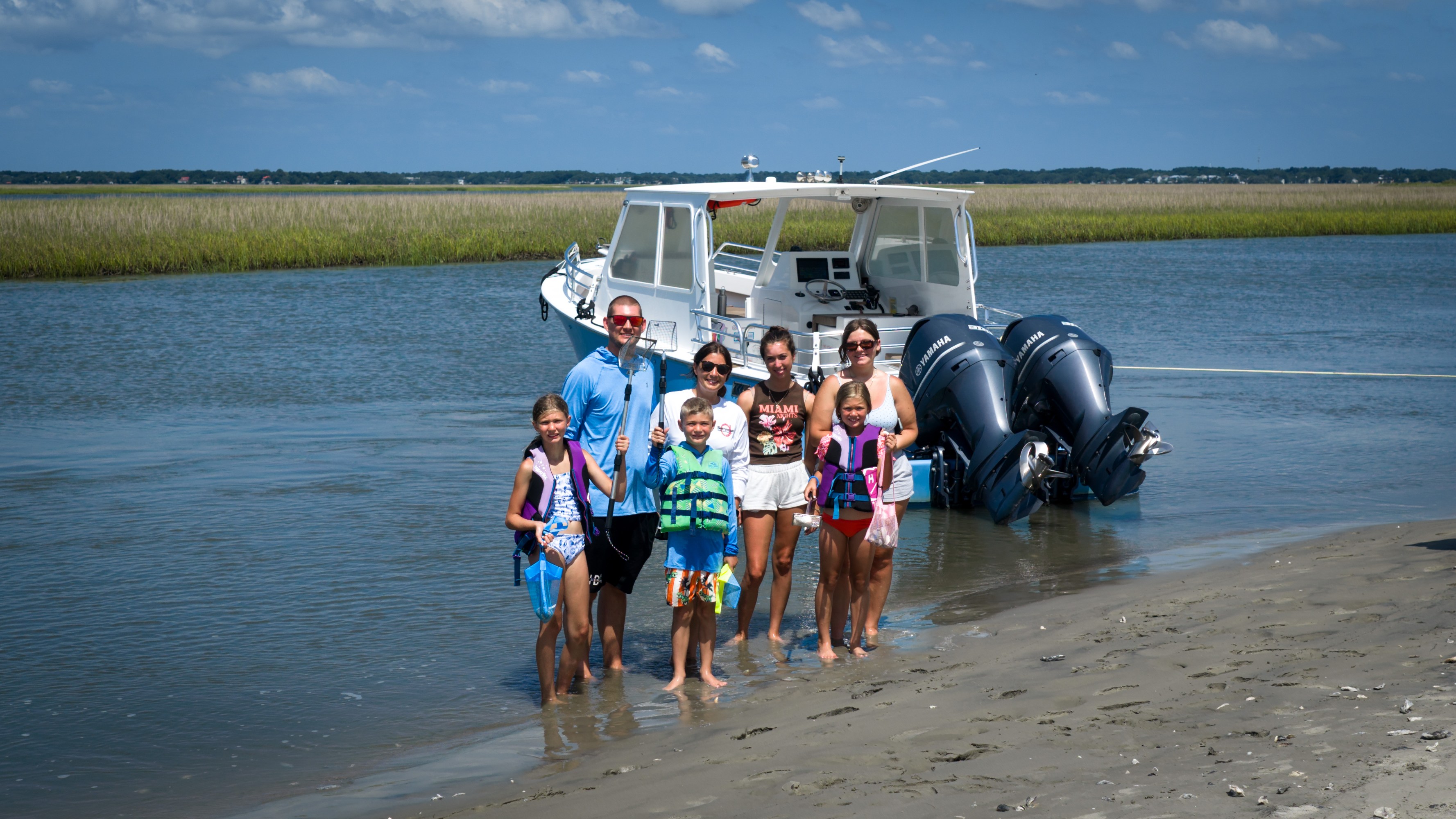 Family standing on sandy shore with a boat in the background.