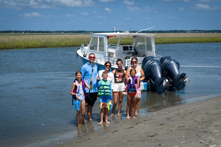 Family standing on sandy shore with a boat in the background.