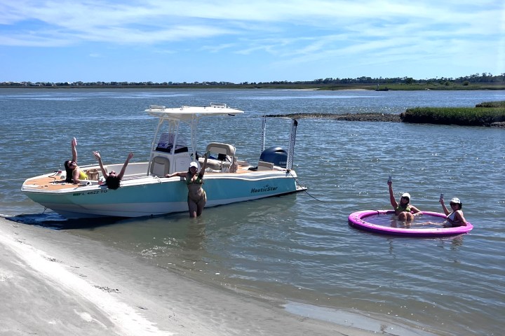 People relaxing on a boat and in a tube on a sunny shoreline.