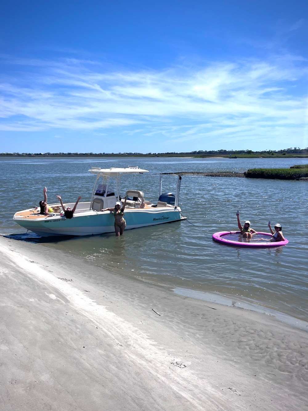 People relaxing on a boat and in a tube on a sunny shoreline.