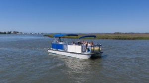 Blue-roofed pontoon boat on a river with passengers under clear sky.