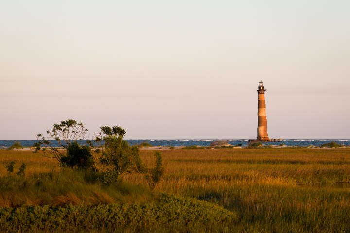 Lighthouse by the ocean with grassy foreground at sunset.