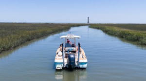 Boat navigating a narrow waterway with a lighthouse in the distance.