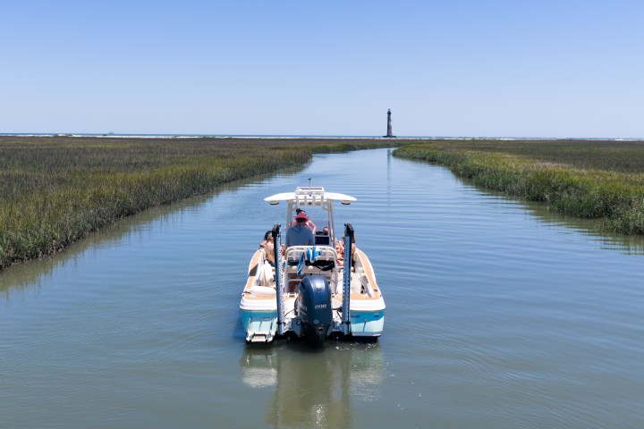 Boat navigating a narrow waterway with a lighthouse in the distance.