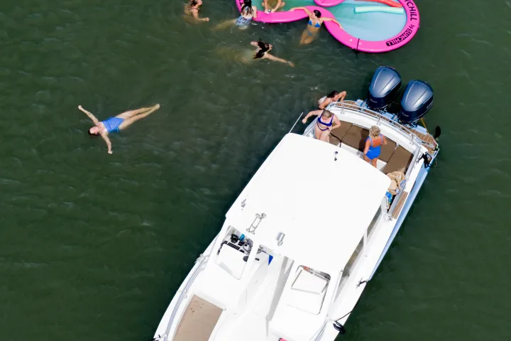 People swimming near a boat and a large pink float in water.
