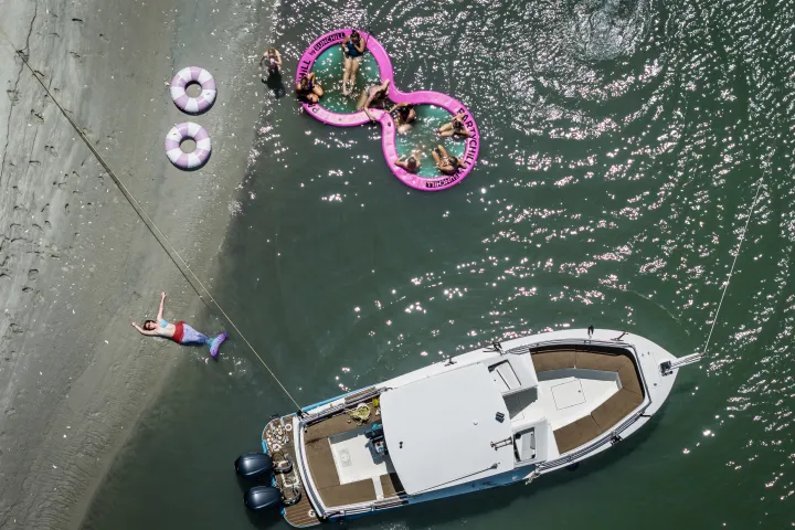 Aerial view of a boat near a beach with people on pink floaties.