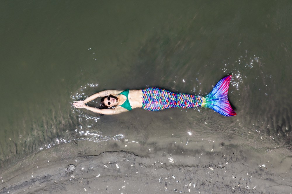 mermaid lying on a sandy beach by the water.